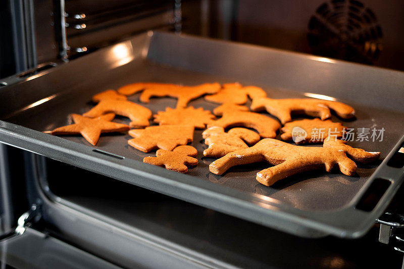 在明亮的厨房里，把圣诞姜饼放在开放式现代烤箱的烤盘上。烤炉里的圣诞饼干——暖暖的灯光，喜庆的气氛。冬季、圣诞节和新年的概念