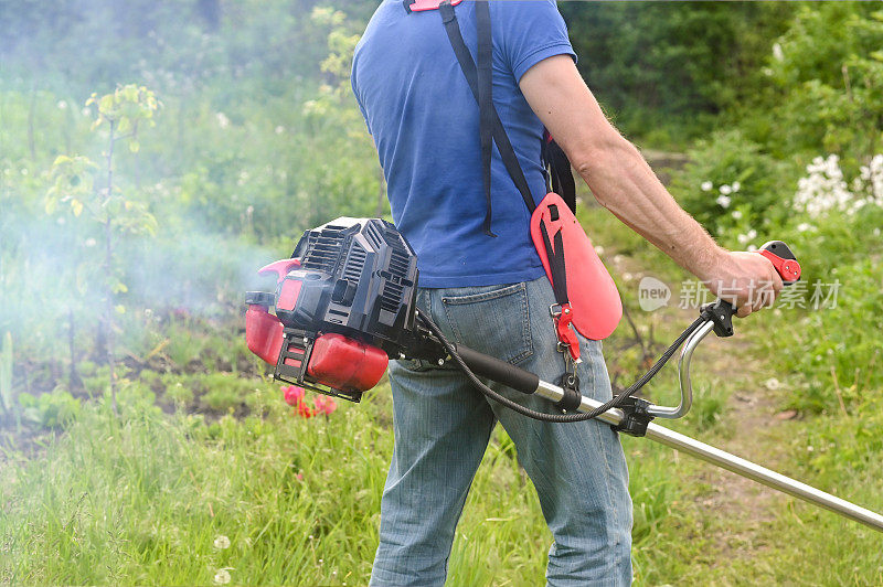 男子在花园或公园用汽油草坪修剪机修剪高草。