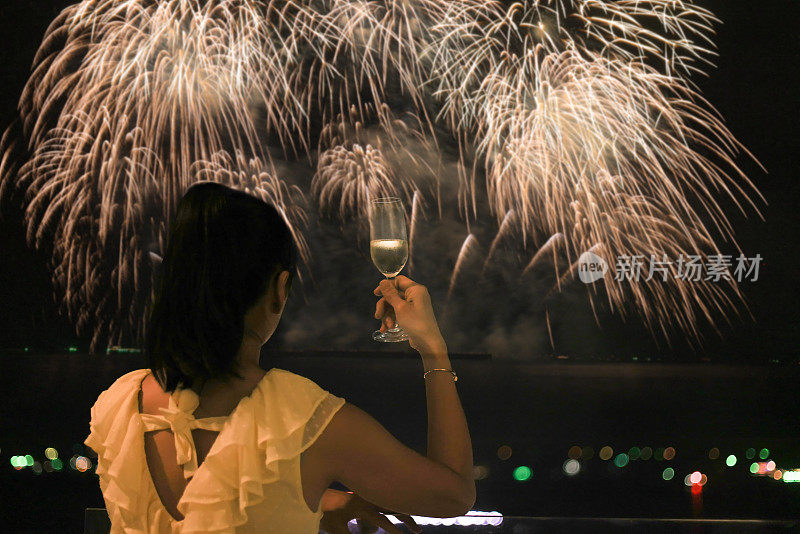 后景:新年之夜，美丽的焰火背景下，女子手里拿着一杯雾气蒙蒙的冰凉香槟