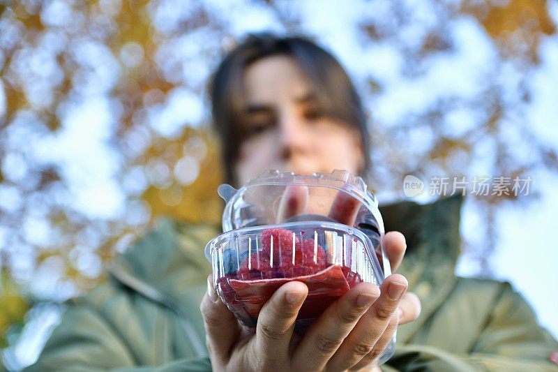 女孩拿着一个塑料盒子，里面装着浆果