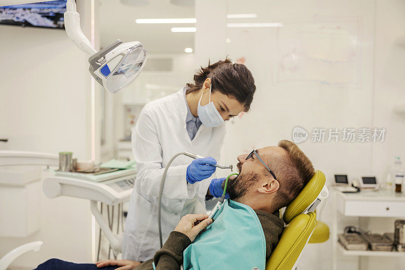 牙医站在诊所里给病人钻牙。
