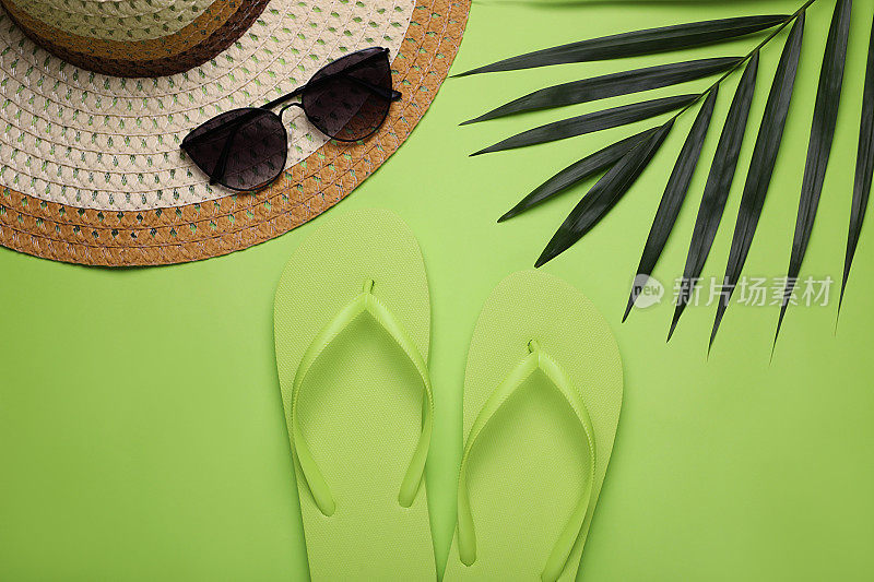 时尚的人字拖，太阳镜，帽子和棕榈叶在浅绿色的背景，平躺
