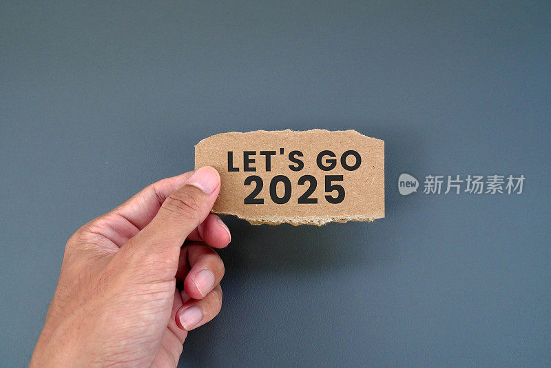 一名男子拿着撕烂的纸板纸条，上面写着“让我们去2025年”。
