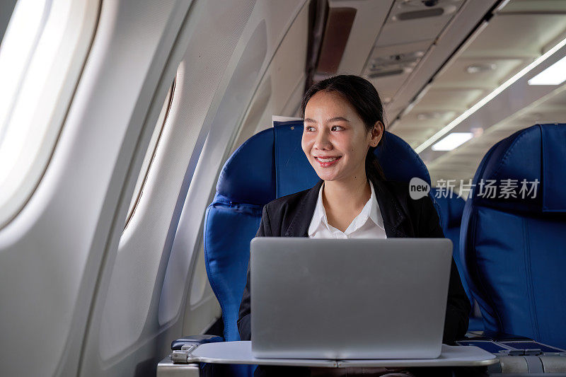 一个年轻的女商人乘商务舱去城外工作。在飞机上用笔记本电脑工作