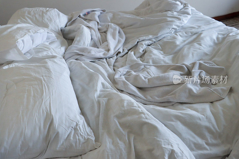 酒店卧室里凌乱的双人床、皱巴巴的床单、皱巴巴的枕头和羽绒被，全景图