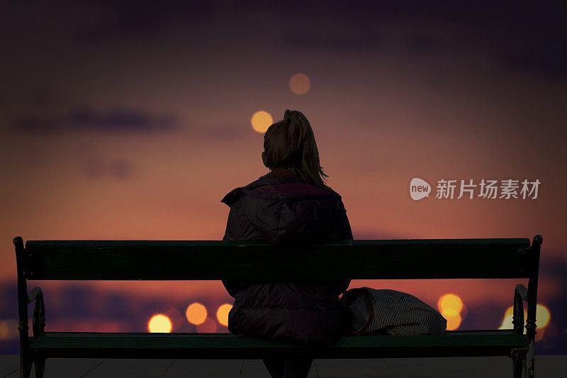 一个女孩的剪影看着城市的灯光散焦