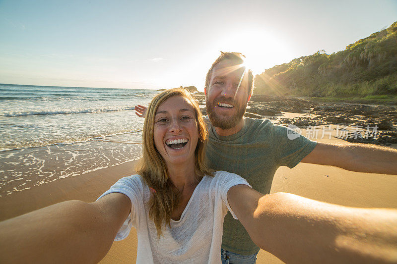 太阳升起时，一对年轻夫妇在海滩上自拍
