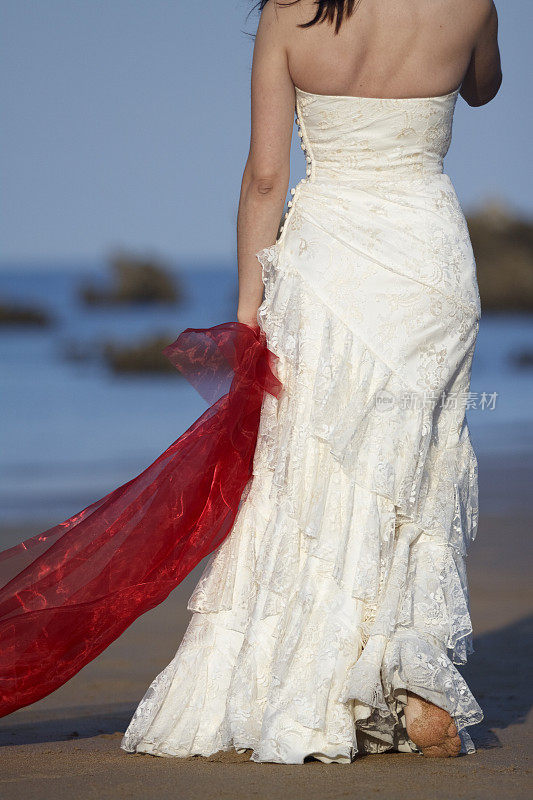 新娘穿着红色薄纱在海滩上散步