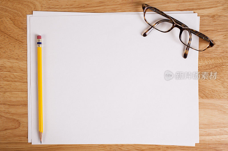 木桌上空白的白纸。眼镜、铅笔。