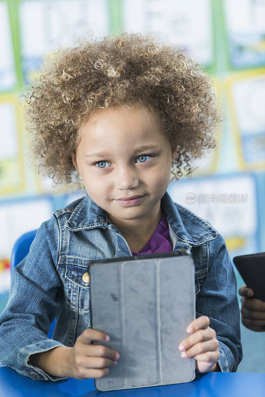 可爱的混血女孩在幼儿园拿着电子平板电脑