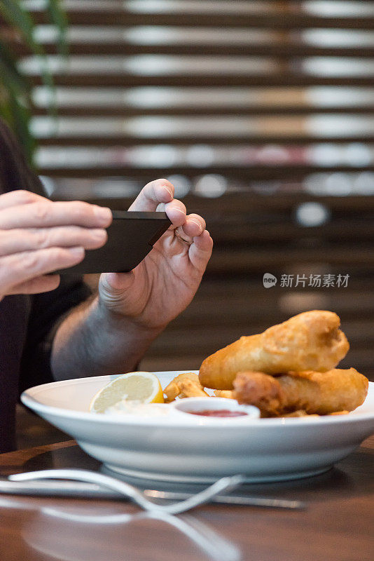 一名男子在餐馆用手机给炸鱼和薯条拍照