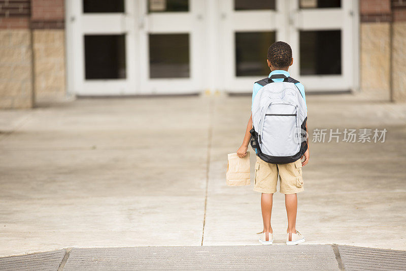 非洲裔，一个小男孩面对着教学楼。午餐,背包。