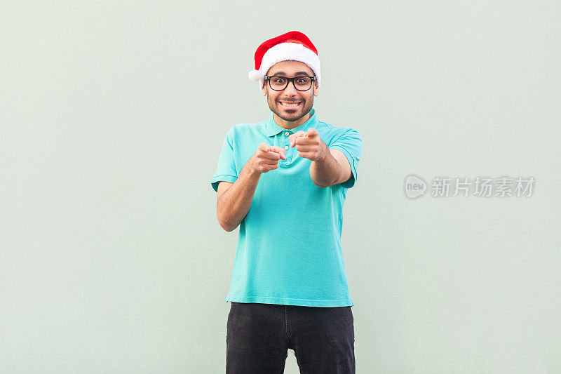 嘿,你!圣诞的人!戴着圣诞帽和眼镜的大胡子男人，指着镜头，露出露齿的微笑。