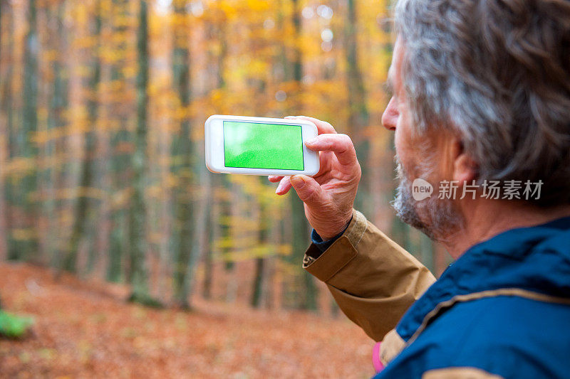 欧洲秋天的森林里，拿着绿屏智能手机的老人