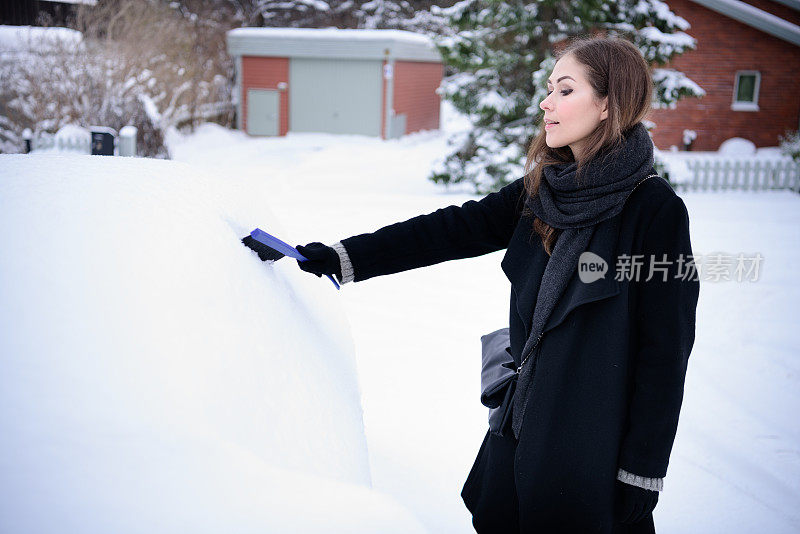 冬天即将来临。女人在冰冷的天气里，车被雪覆盖着。