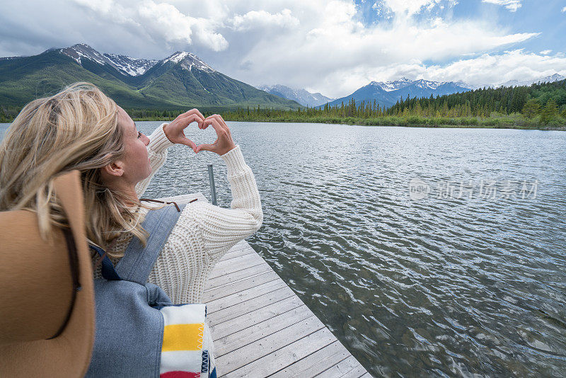 年轻女子在山湖上做心形手指架