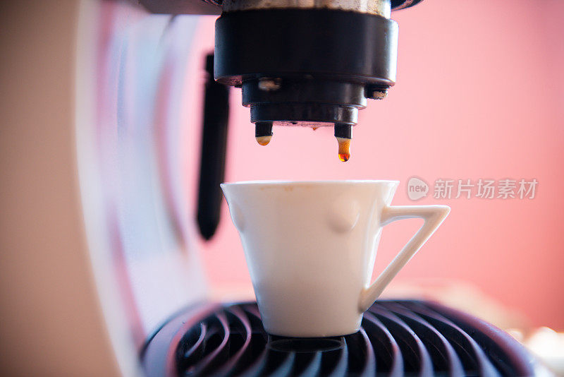 浓缩咖啡被倒入一个杯子从一个浓缩咖啡机，特写，粉红色的背景