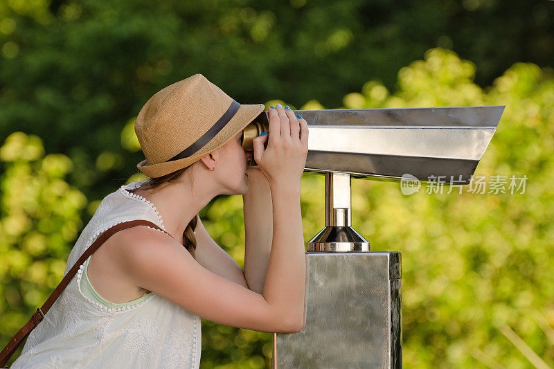 戴帽子的女孩看着大望远镜。背景中的公园