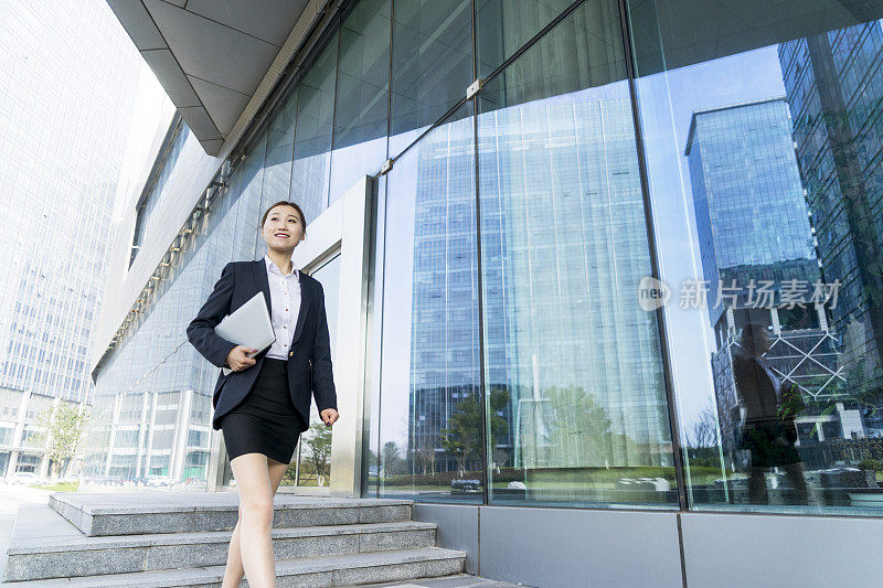 一名女商人拿着笔记本电脑在城市中行走