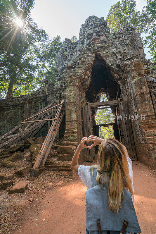 一个年轻女子在柬埔寨旅行，喜欢吴哥窟的庙宇，用手做一个心形的手指框架。