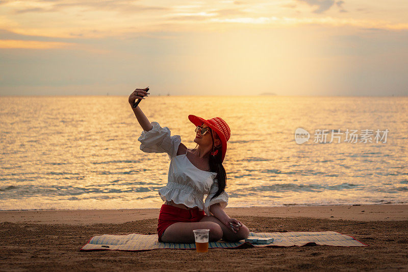 美丽的女人躺在垫子和幸福的沙滩上，放松地看日落和自拍