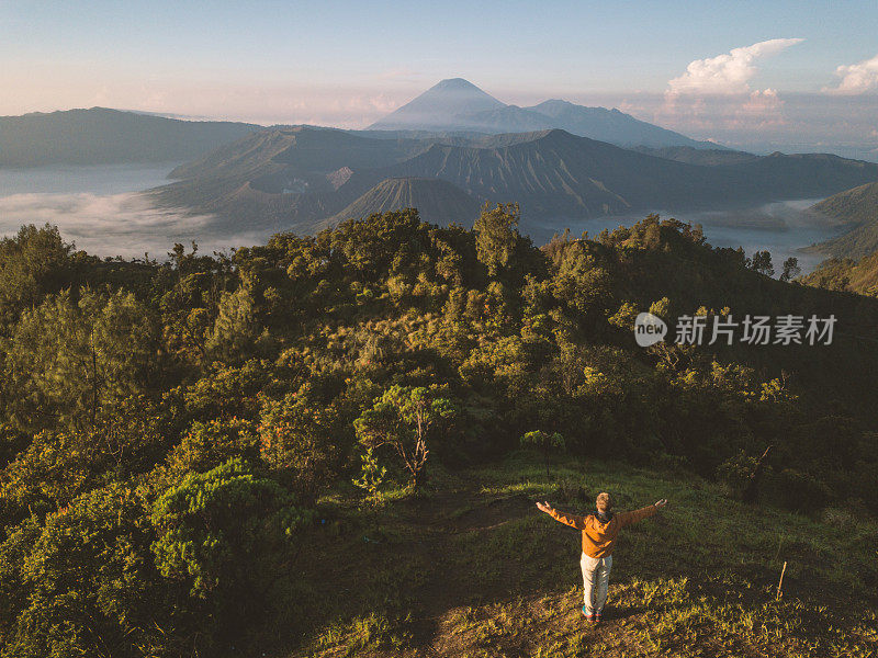 无人机航拍的年轻男子徒步旅行与Bromo火山的观点在印度尼西亚站在山顶手臂张开-人们旅行有趣的冒险概念成功和成就