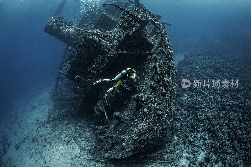 潜水员在一艘被珊瑚和海藻完全覆盖和消耗的大型沉船附近潜水，在红海的底部