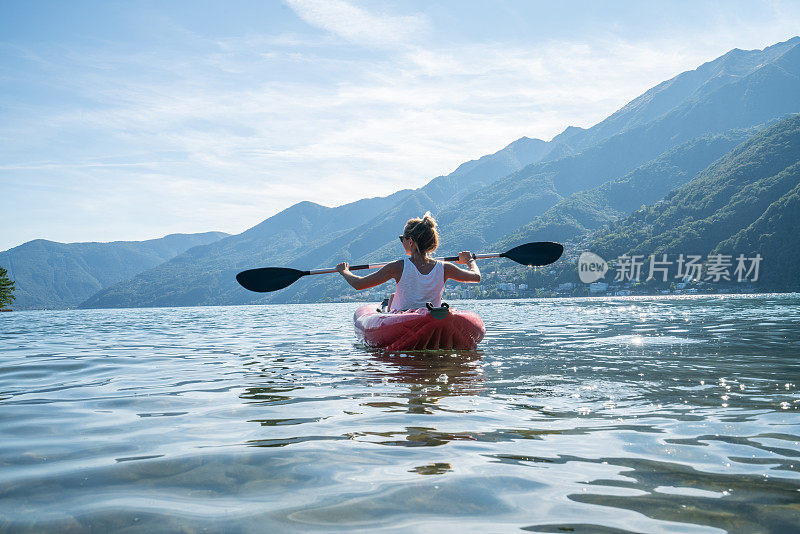 年轻女子在山湖上划着红色的独木舟