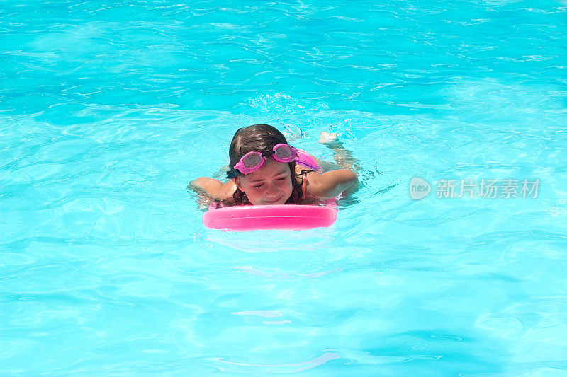可爱的小女孩在游泳池里的踢板上练习游泳