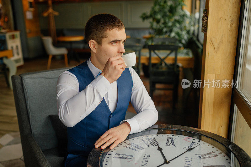 婚礼当天，新郎坐在阁楼内部的椅子上，喝着咖啡，看着窗外。新郎的肖像。