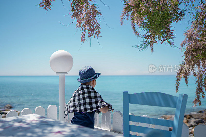 可爱的男孩站在餐厅的露台上欣赏风景