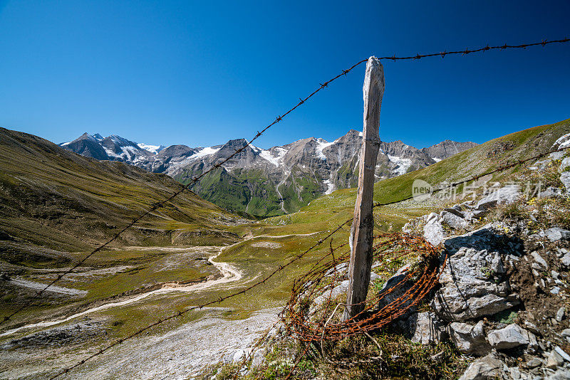 锈迹斑斑的带刺铁丝网栅栏在高高山牧场，以大格洛克纳山脉的视野