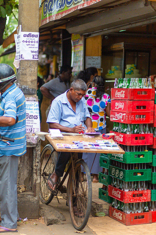 一个骑自行车的人在市场上卖彩票。斯里兰卡的贫穷和苦难
