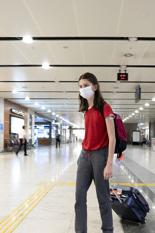 一个带着医用口罩的小女孩在机场散步。