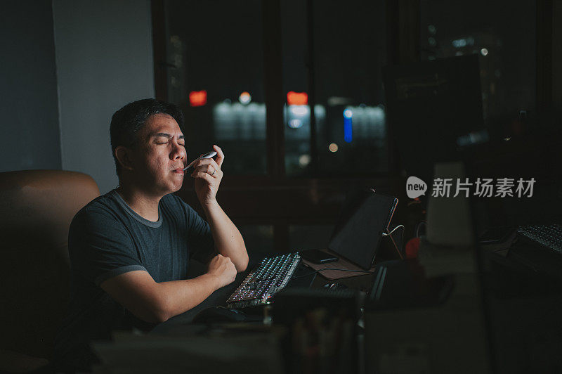 一名亚裔华人中年男子在自习室里，在台式机前发烧，用体温计测体温