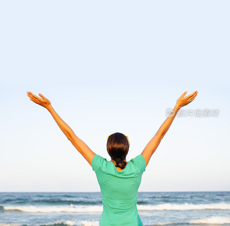 沙滩上的女孩以大海为背景举起双手。