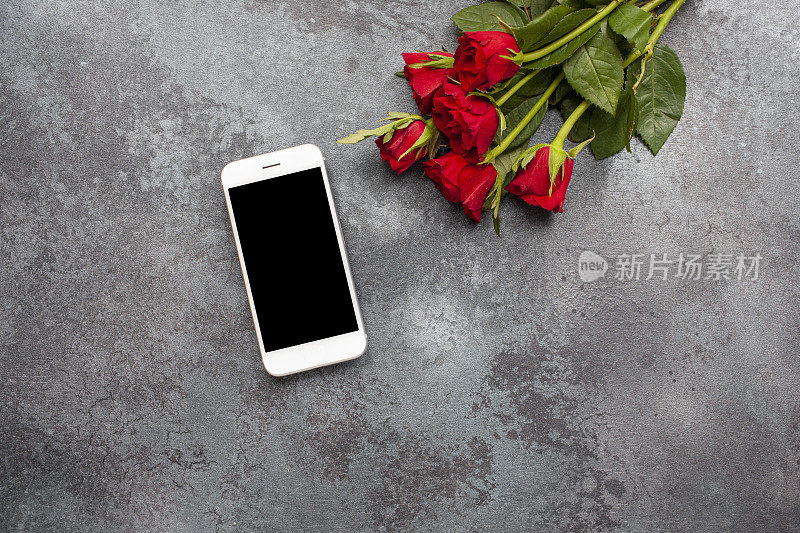 俯视图手机模板与玫瑰在黑暗的纹理背景与复制空间