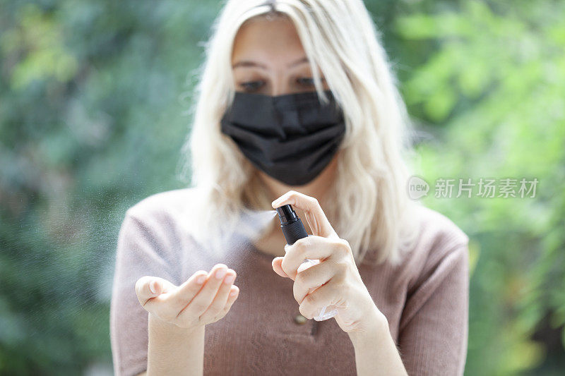 戴黑色口罩的妇女使用消毒剂对抗病毒