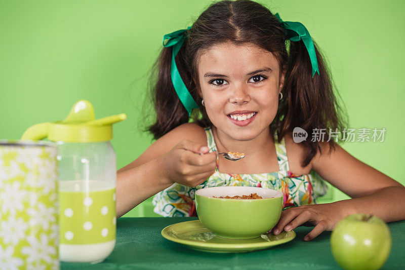 快乐的女孩一边吃早餐麦片，一边对着镜头微笑