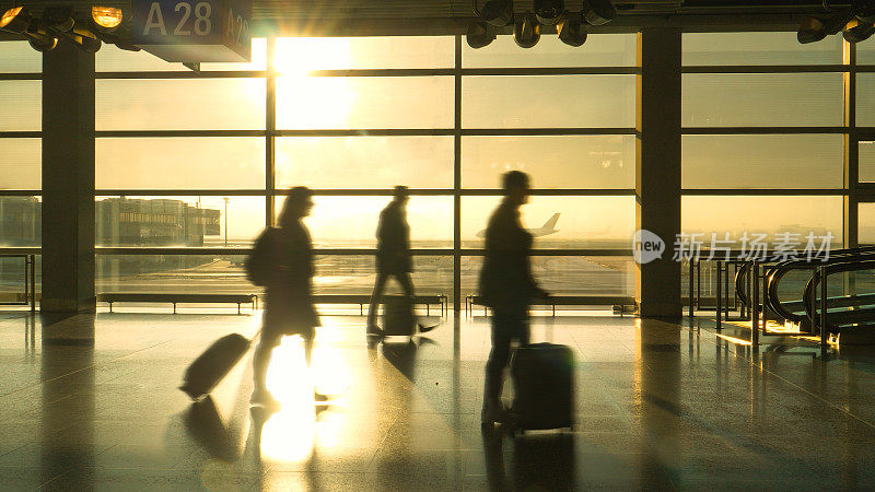 剪影:通勤者带着他们的行李箱匆匆穿过繁忙的机场终点站。
