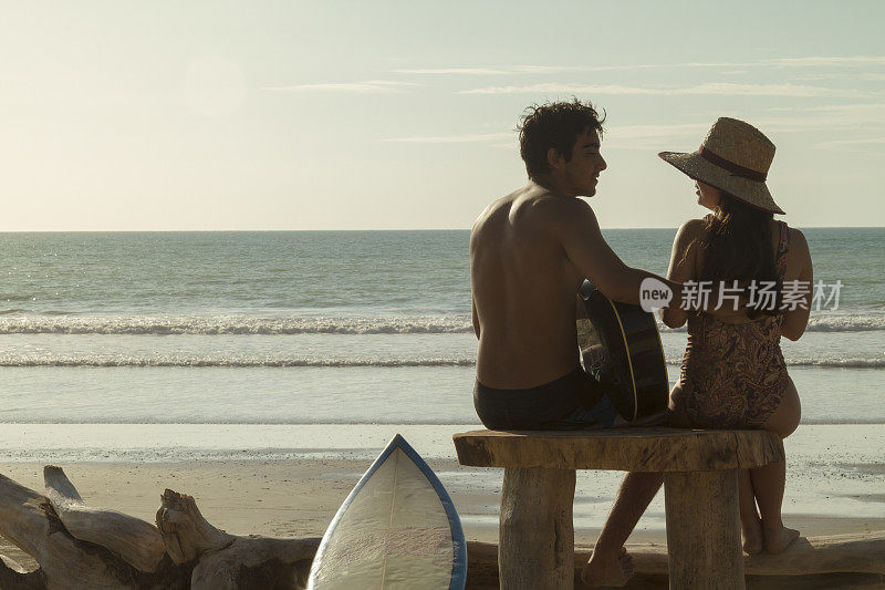 一对拉丁健美的异性恋冲浪者夫妇，在大海前弹奏原声吉他，放松在卡诺阿，Manabi省，厄瓜多尔，拉丁美洲