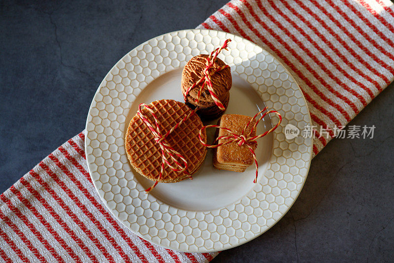 将饼干和焦糖华夫饼绑在米色盘子上，在红色米色条纹餐巾的黑色背景上