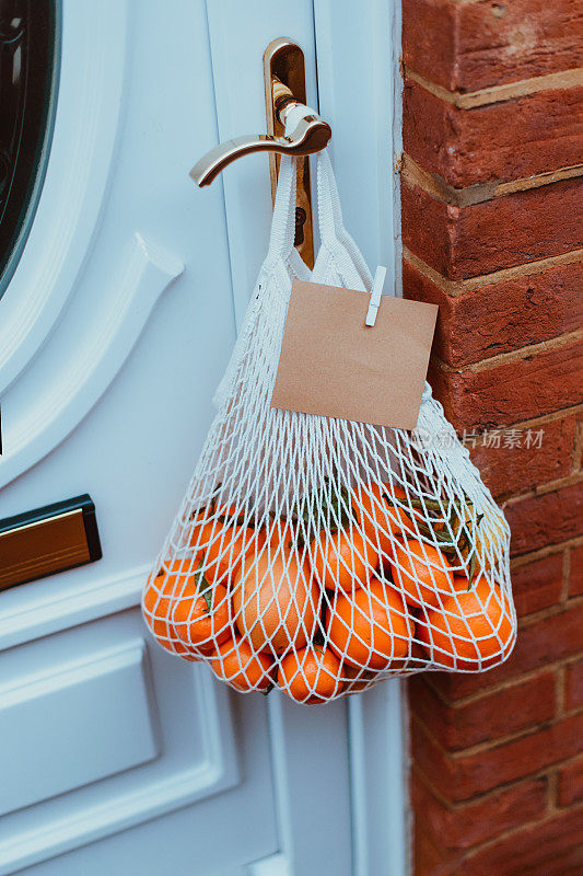 环保材料制成的可重复使用的绳袋，有柑橘类水果，门把手上挂着空白卡片。当地农民健康食品配送。零废品,塑料的生活方式。