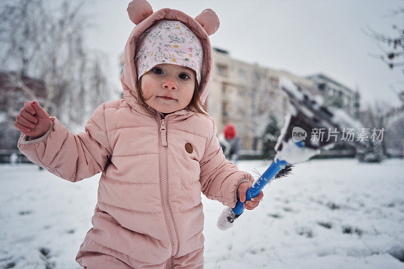 可爱的蹒跚学步的小女孩拿着塑料刮冰器探索下雪天