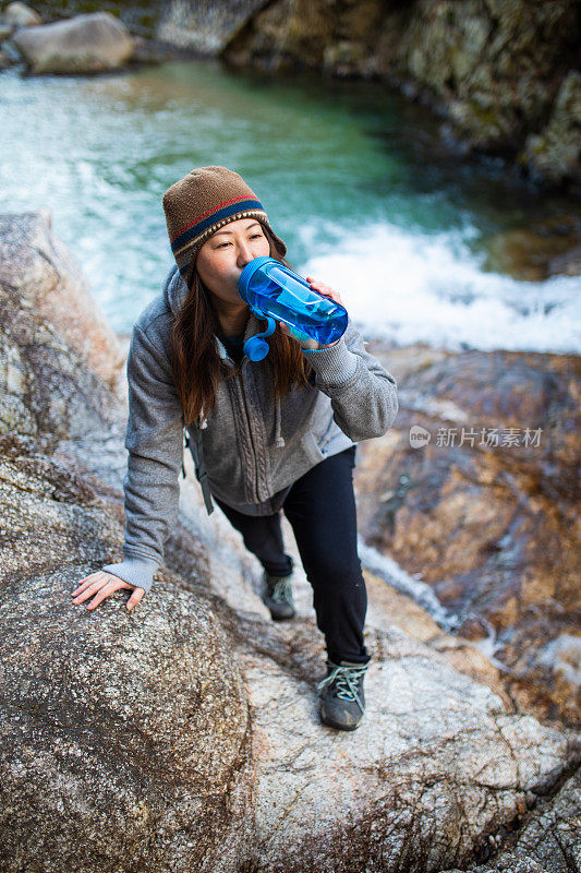 一个女人爬上河边的悬崖停下来喝水