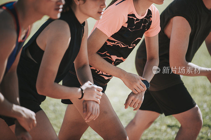 亚洲华人运动员在晨跑前用健身追踪器排队准备计时，并跑向田径赛场的终点线