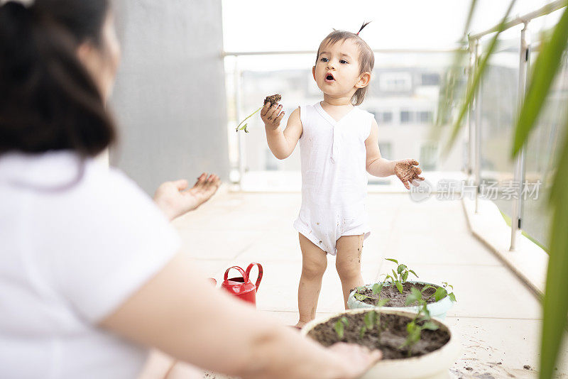 年轻的妈妈和她可爱的小女儿在自家阳台上种花