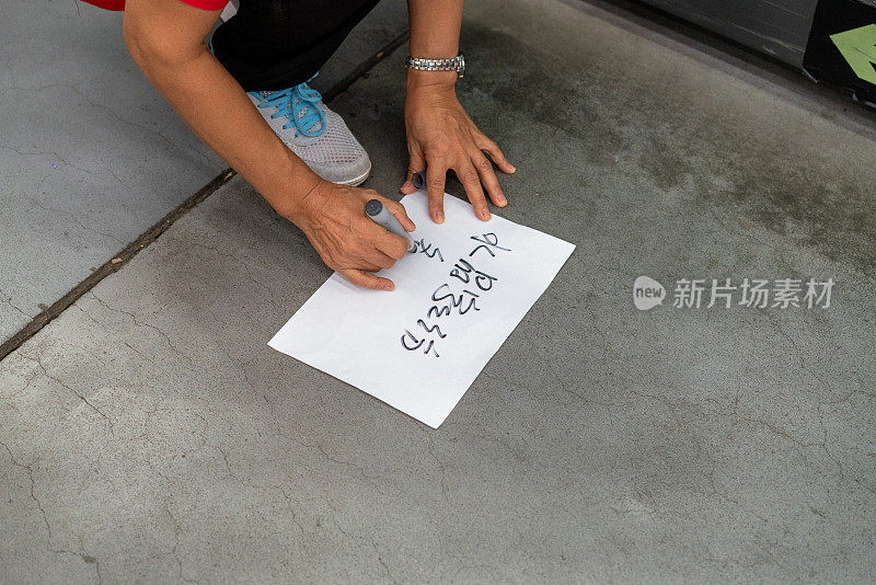 一个女人蹲在地上，用笔在纸上写字，她的手特写