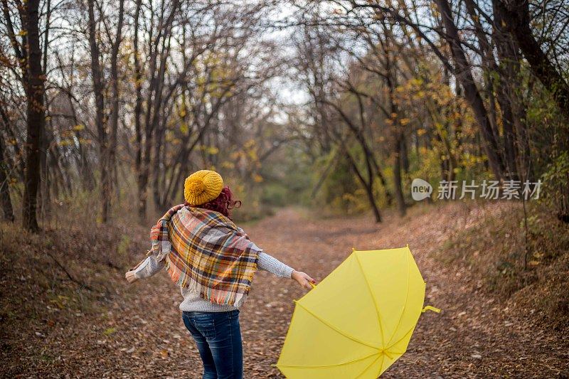 一个女人拿着黄色的伞在公园里散步