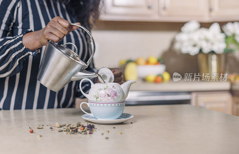 一名成熟迷人的非洲裔美国黑人女性正在把茶壶里的茶倒到茶壶里。